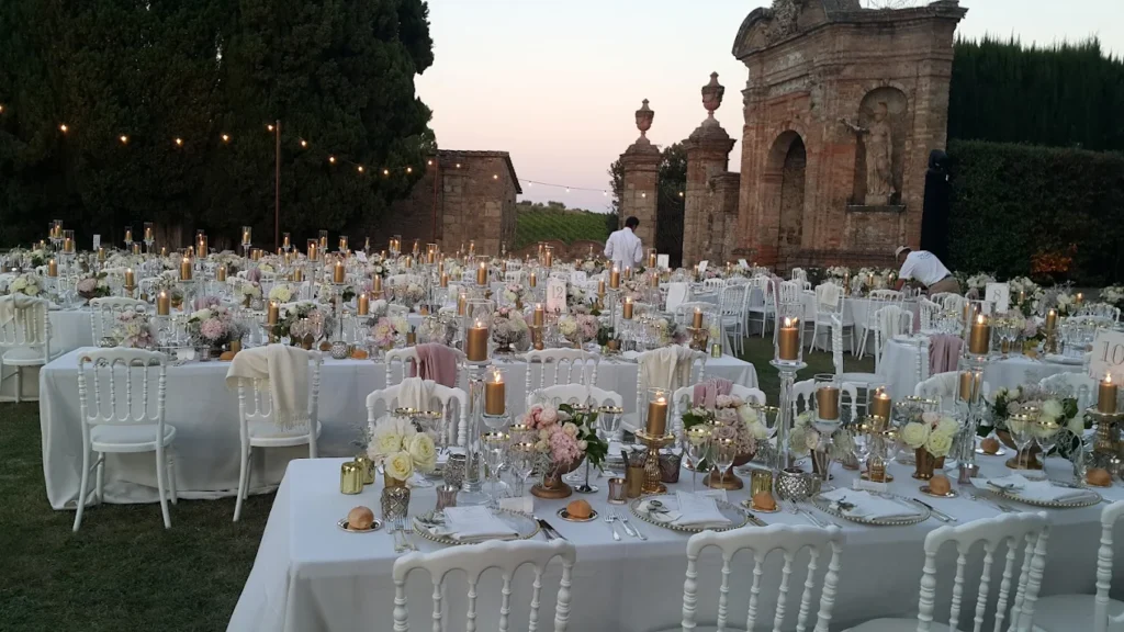 Wedding photographer in Tuscany/wedding media production in Italy. Elegant outdoor wedding dinner setup at Villa di Geggiano in Tuscany with long white tables, candles and floral arrangements at sunset.