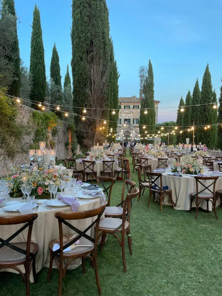 Wedding photographer in Tuscany: Outdoor wedding dinner at Villa Centinale with string lights, floral centerpieces and Tuscan cypress trees.