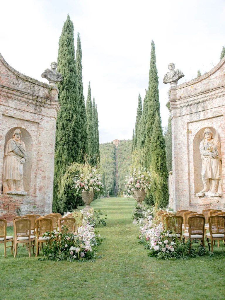 Wedding photographer in Tuscany: Romantic wedding ceremony aisle framed by cypress trees and classical statues at Villa Cetinale in Tuscany.