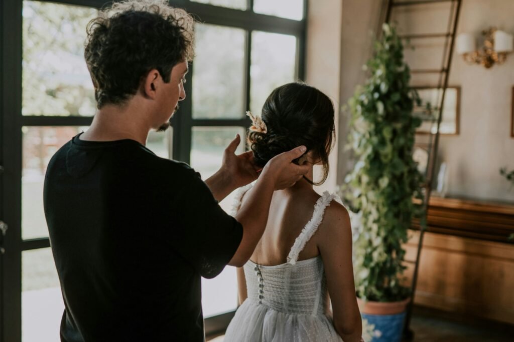 Bride getting ready with stylist adjusting her hair in natural light.