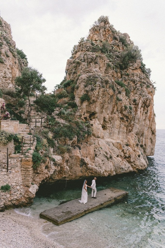 Wedding venues in Sicily Italy by the coast. Married couple standing by the sea at Tonnara di Scopello on the coast of Sicily.